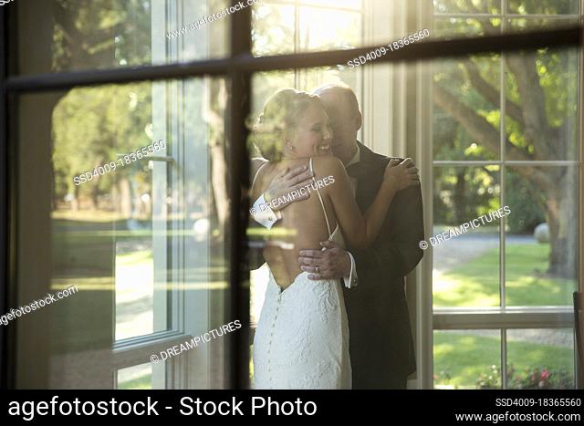 Bride and father of the bride embracing celebrating the wedding day, seen through window