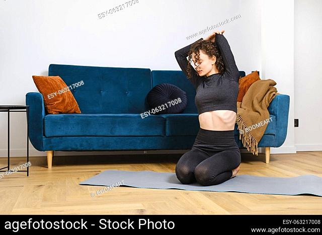 Young woman warming up back muscles sitting on the mat and doing fitness exercises at home