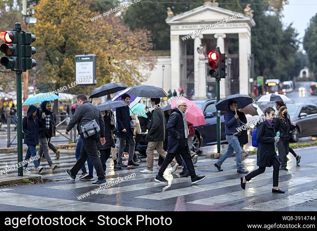 Rome, Italy: People in the city cross the street protecting themselves from the rain with umbrellas. Citizens in the rain