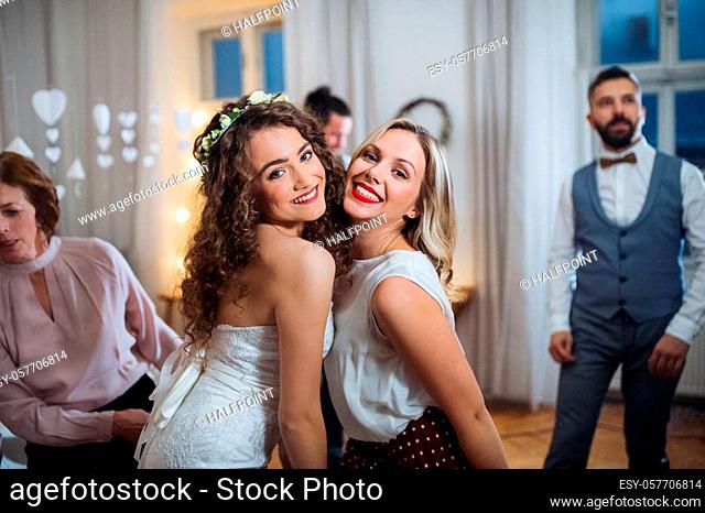 A portrait of young bride and her female friend or sister posing for a photograph on a wedding reception when dancing