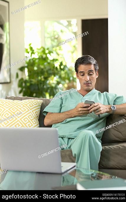 Hispanic Male doctor practicing tele-medicine from his home, using cell phone and laptop computer, Listening to patient on video call