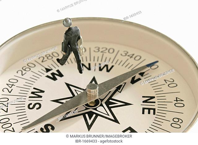Miniature business man figure walking west on a compass which is pointing north, symbolic image for deviating from the course