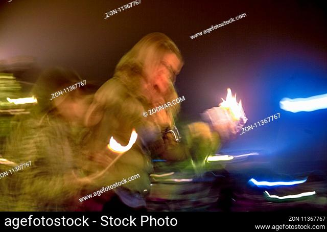 A blurred image of people with candles in their hands mourning or celebrating outdoors. Night
