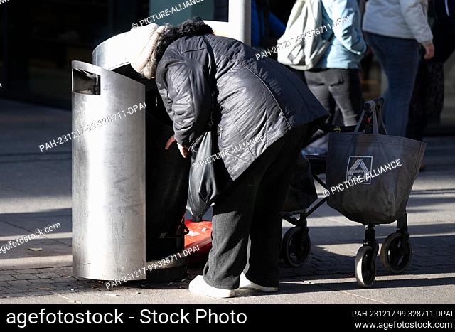17 December 2023, Saxony, Dresden: A woman searches for empties in a garbage can. Photo: Sebastian Kahnert/dpa. - Dresden/Saxony/Germany