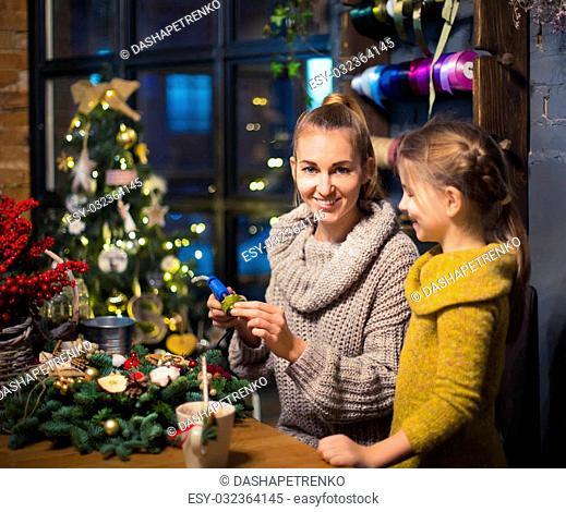 Mother and daughter decorating coniferous wreath. Christmas celebration concept