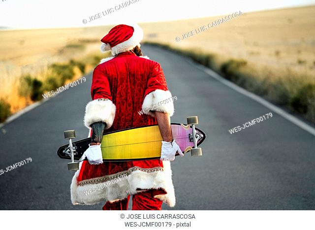 Rear view of Santa Claus holding a longboard on country road