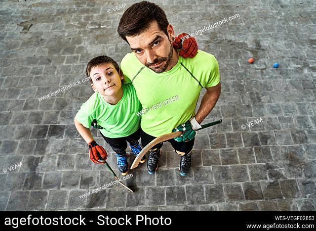 Boy with arm around father holding sticks at hockey court