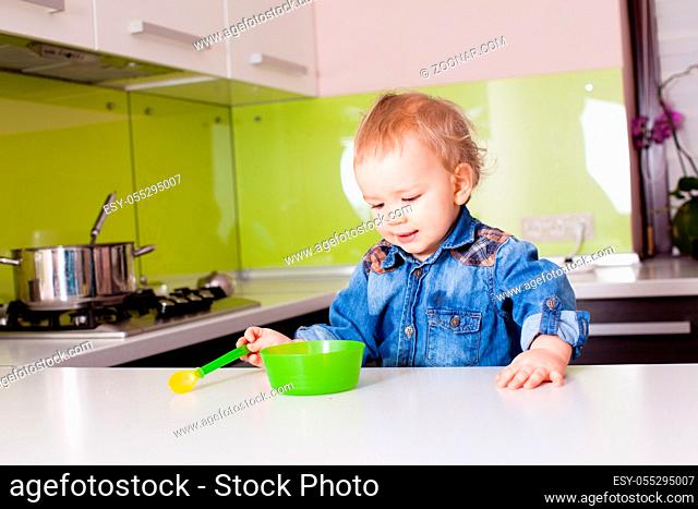 Small baby boy eating by himself using spoon. Baby boy looking on the green plate