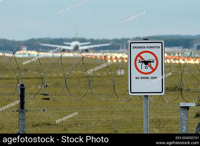Waning sign NO DRONE ZONE at the fence of german airport with blurry passenger airplane in the background