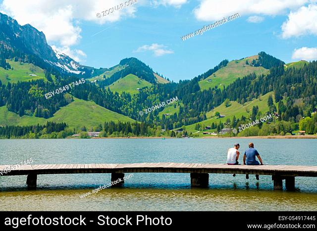 Schwarzsee, FR / Switzerland - 1 June 2019: two men best friends enjoy the summer lakeside view at the Schwarzsee Lake in the Swiss Alps in canton Fribourg