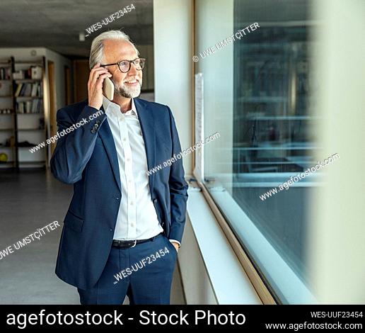 Male entrepreneur with hand in pocket talking on smart phone at office