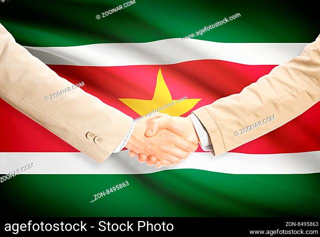 Businessmen shaking hands with flag on background - Surinam