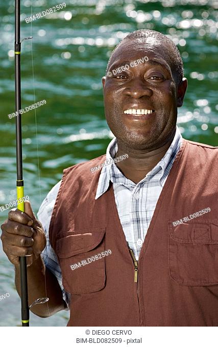 Black man holding fishing rod near stream