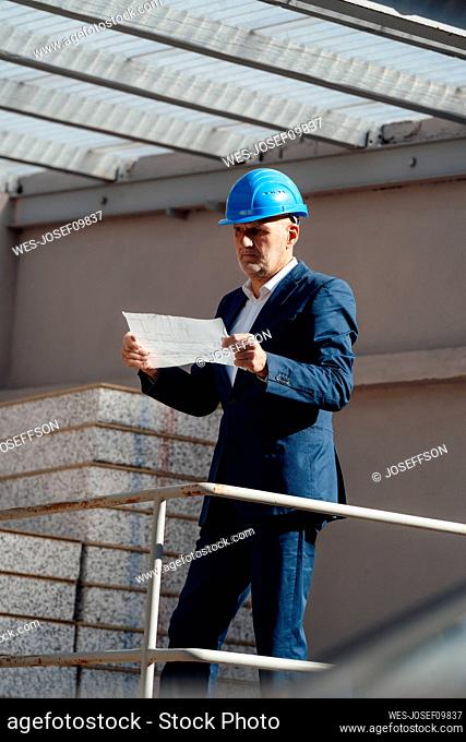 Architect wearing hardhat examining blueprint at construction site