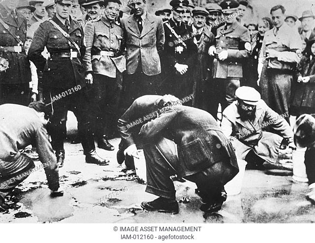 Austrian Nazis and local residents look on as Jews are forced to get on their hands and knees and scrub the pavement, 1938