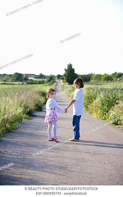 A boy and a girl hand in hand walking on a country road