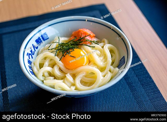 A dish of noodles, vegetables and fish with a yellow egg yolk