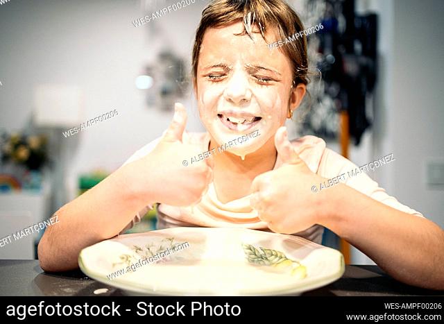 Smiling girl showing thumbs up while face smeared with flour and water