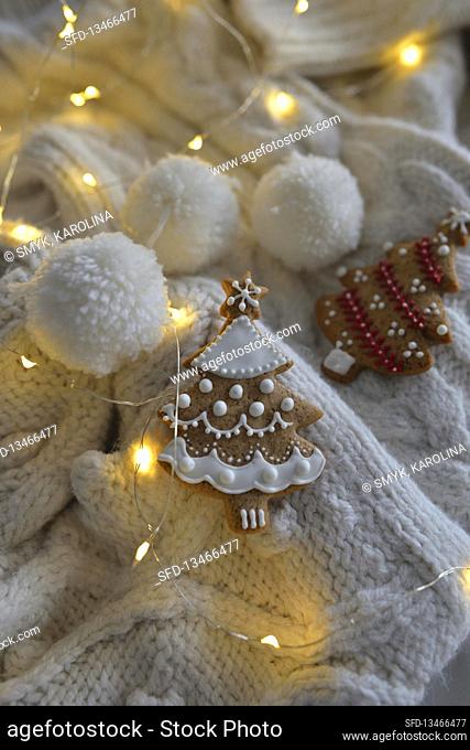 Gingerbread fir tree with fairy lights and pompoms on a white knitted blanket