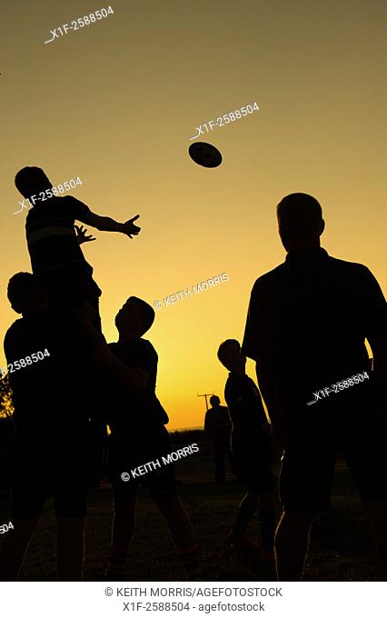 Silhouettes of young teenage men boys taking part in rugby training coaching practicing lineout ball handling, at dusk, Aberaeron Wales UK