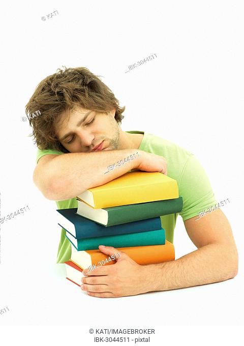 Young male student with a stack of books, tired, exhausted, asleep