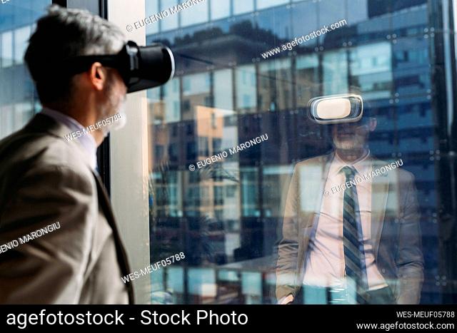 Mature businessman wearing virtual reality simulator standing in front of window