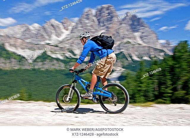 Man mountain biking from Tonde De Faloria to Rio Gere with Cima De Meso Cristallo in the background high above the city of Cortina in northern Italy