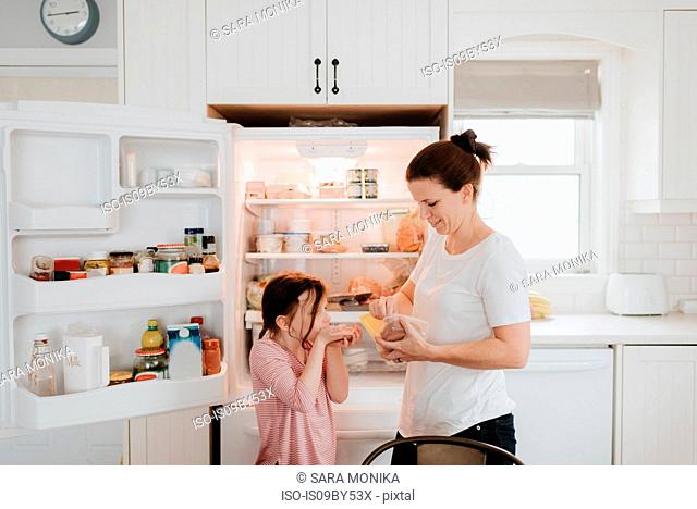 Mother giving daughter cold meat from fridge