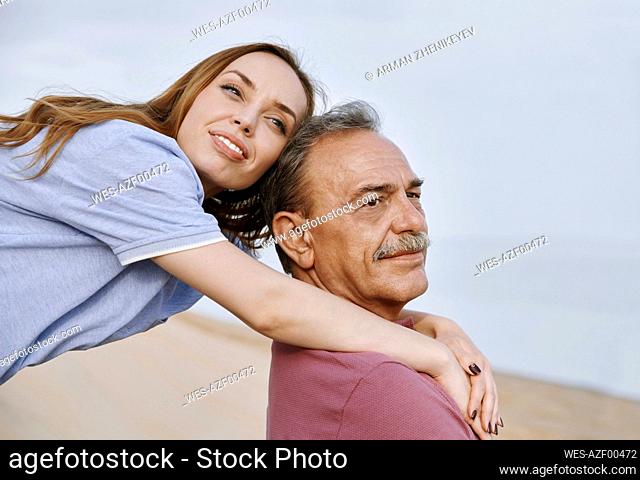 Thoughtful daughter arm around with father sitting at beach