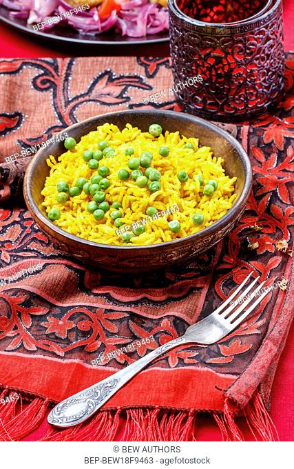 Indian cuisine: bowl of yellow rice with green peas on red background