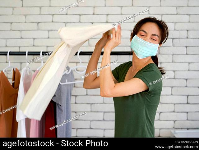 An Asian laundry worker wearing a mask while shaking the cloth before hanging. Working atmosphere in the laundry room. Concept of new normal business during...