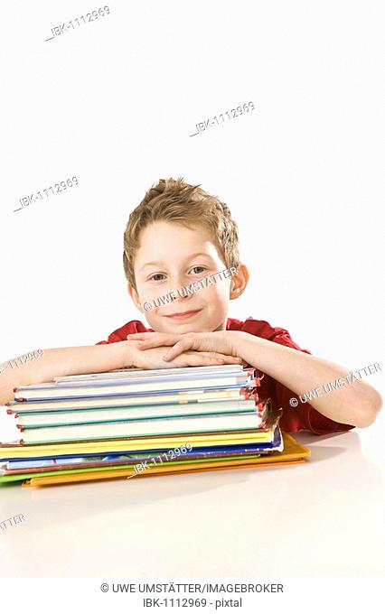 Smiling boy sitting in front of a pile of exercise books and school books