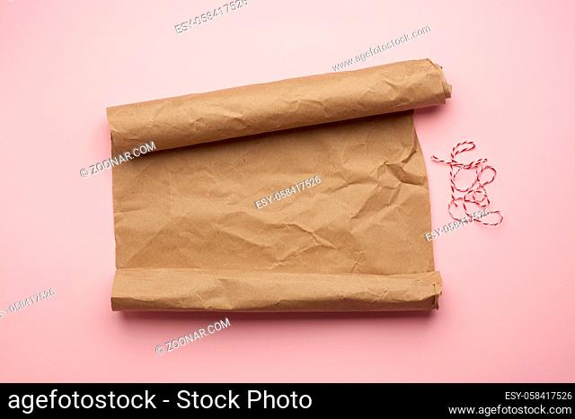 untwisted roll of brown paper on pink background, top view, copy space