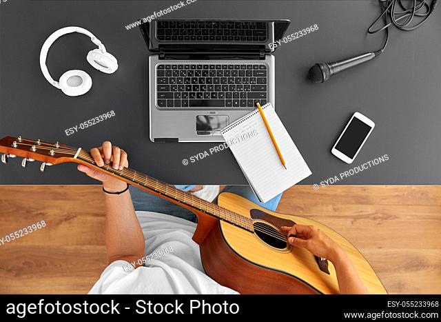 young man with laptop playing guitar at table