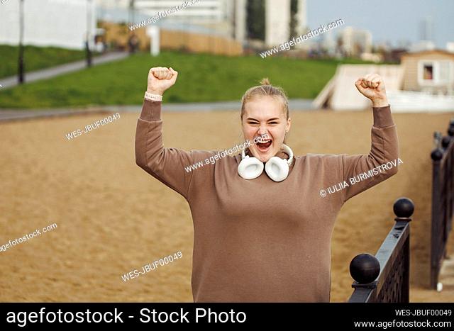 Cheerful woman with headphones standing by railing