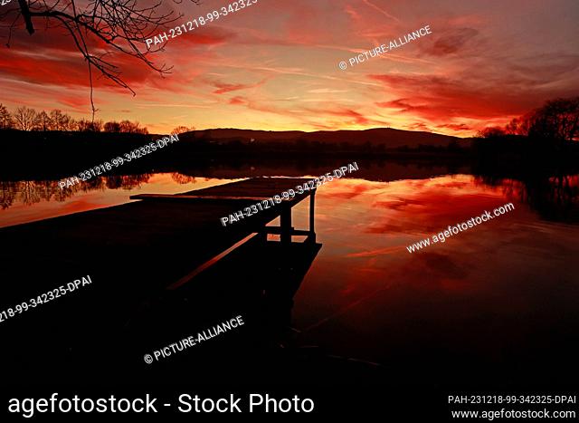 18 December 2023, Saxony-Anhalt, Wernigerode: In the light of the setting sun, the Harz mountains with the Brocken are reflected in a pond near Wernigerode