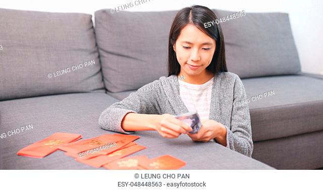 Woman putting money banknote into red packet at home