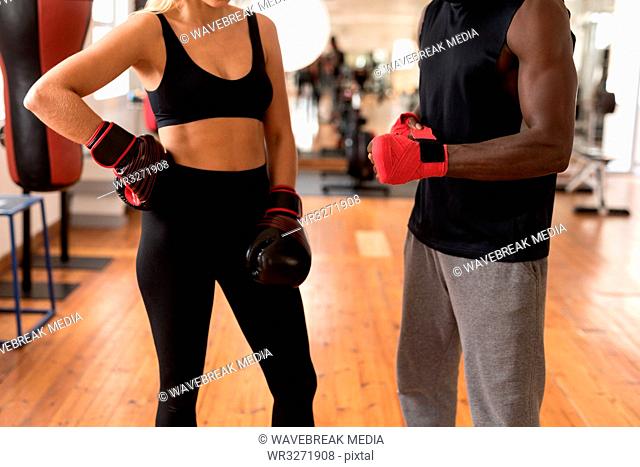 Male trainer assisting female boxer in fitness studio