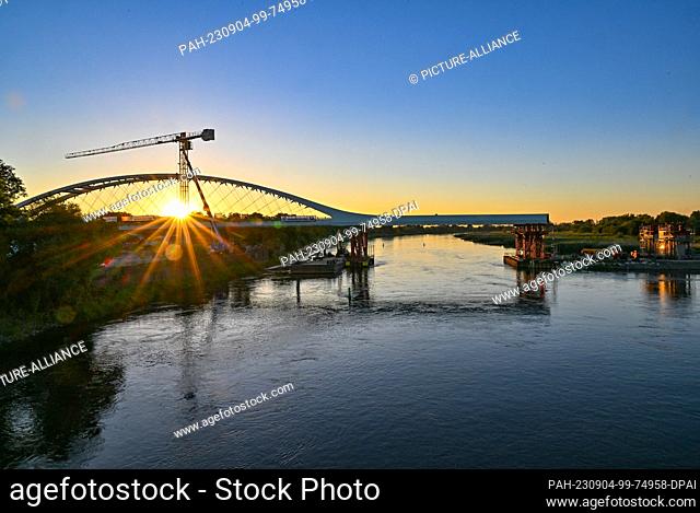 04 September 2023, Brandenburg, Küstrin-Kietz: The sunset shines over the German-Polish border river Oder with the new railroad bridge