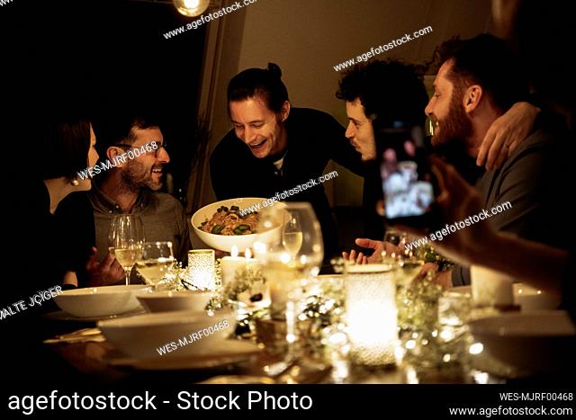 Smiling man showing pasta to male and female friends at dining table