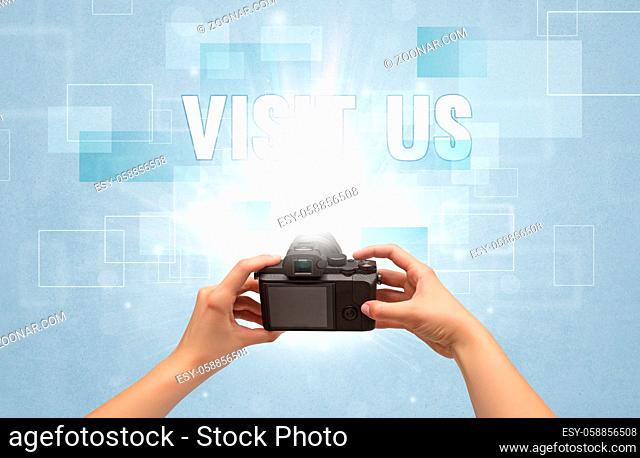 Close-up of a hand holding digital camera with VISIT US inscription, traveling concept