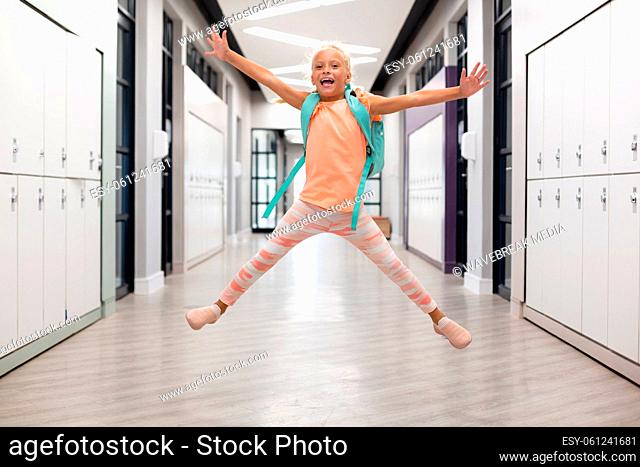 Full length of caucasian elementary schoolgirl with arms outstretched jumping in corridor
