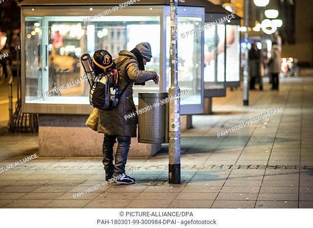 28 February 2018, Germany, Frankfurt am Main: A homeless person searches for returnable bottles in a waste bin at temperatures below zero degrees