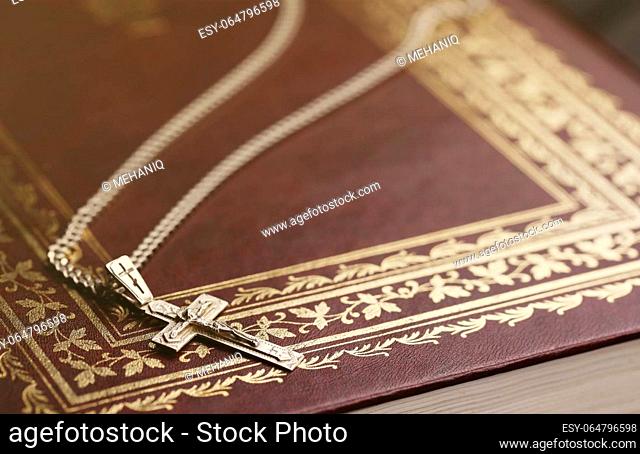 Silver necklace with crucifix cross on christian holy bible book on black wooden table. Asking blessings from God with the power of holiness, which brings luck