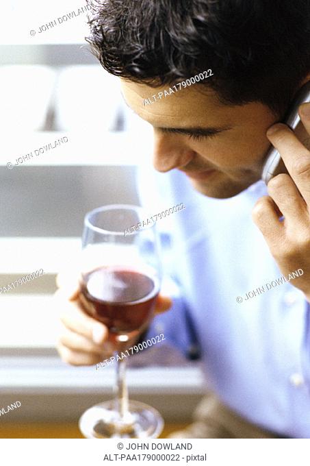 Man using cell phone, holding wine glass, close-up