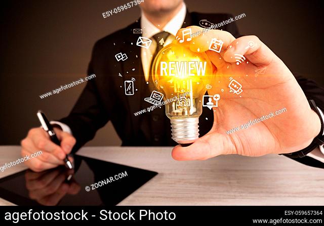 Businessman holding light bulb with REVIEW inscription, social media concept
