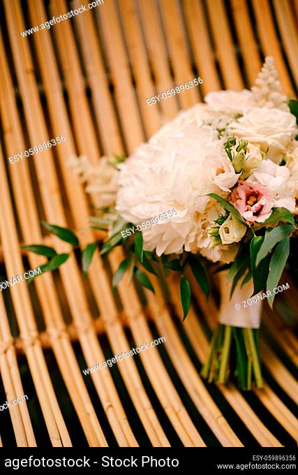 bridal bouquet of white peonies, roses, pink eustoma, astilbe and branches of eucalypt tree on a straw chair. High quality photo