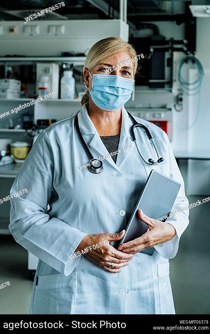 Scientist with face mask and digital tablet standing at laboratory