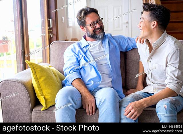 Happy father and son talking while sitting on sofa at home. Cheerful father with teenage son sitting on couch in the living room of apartment