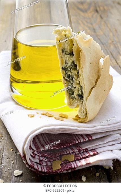 A piece of spinach and ricotta pie beside bottle of olive oil